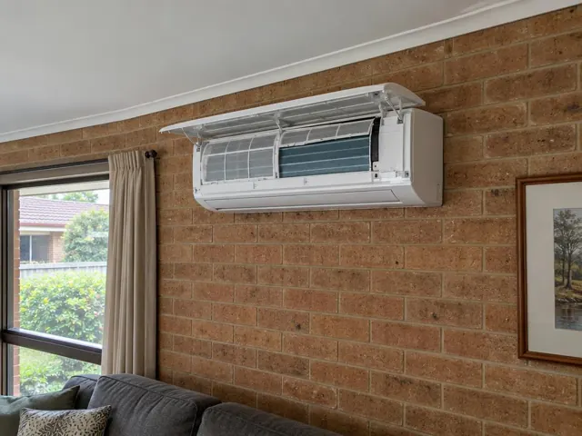 Clean split system with open front panel and visible filters on a brick living room wall in Clearview
