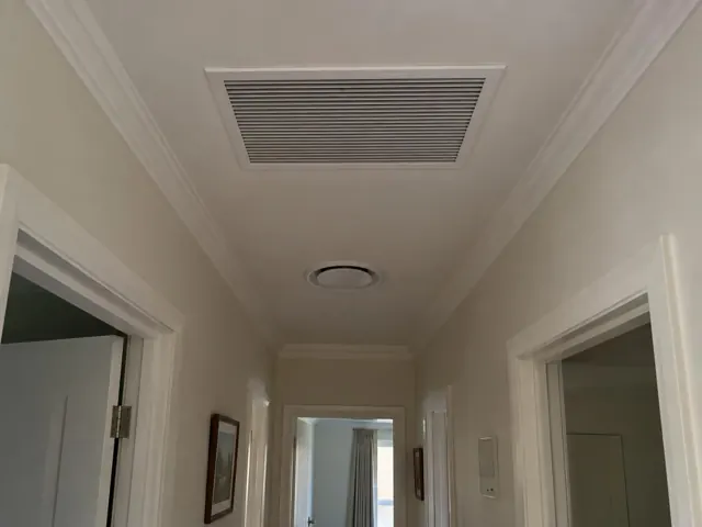 Ceiling ducted air grille and wall controller in a narrow hallway with white trim in Prospect