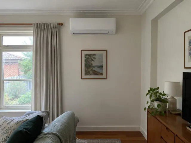 Wall-mounted split system above framed artwork in a living room with curtains and timber floor in Kilburn